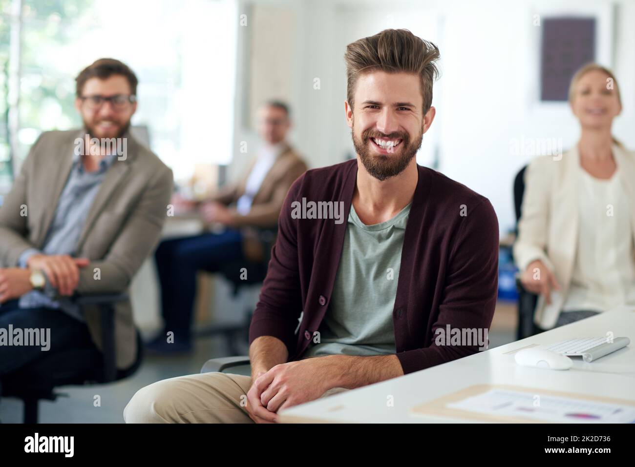 Moderne Führung sieht vielversprechend aus. Lächelnder kreativer Profi mit Kollegen im Hintergrund. Stockfoto