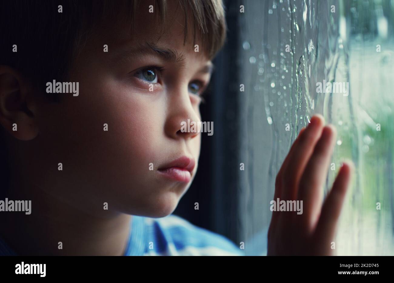 Wenn die Natur Ihren Plan zum Spaß sabotiert. Aufnahme eines traurigen Jungen, der den Regen durch ein Fenster zu Hause beobachtete. Stockfoto