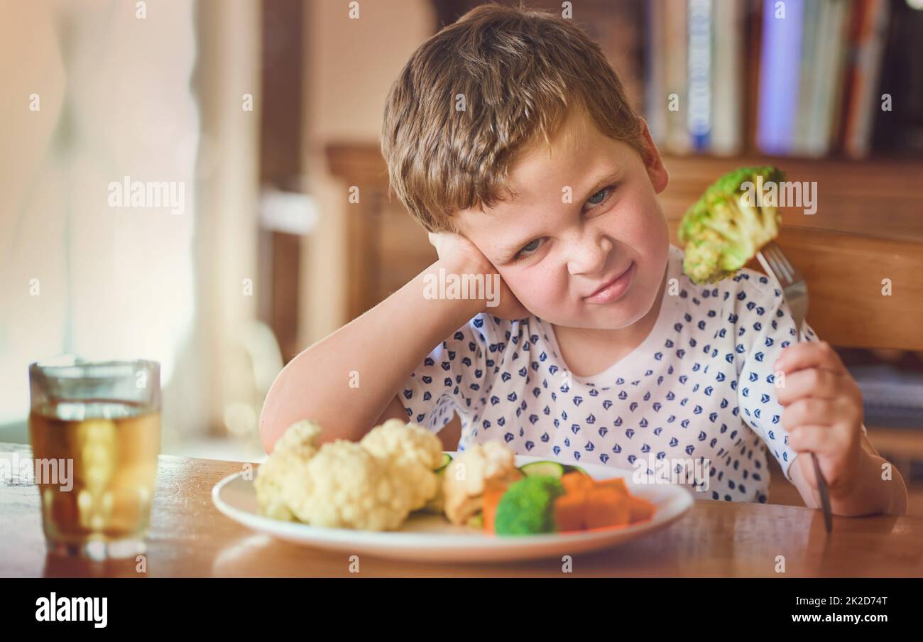 Es gibt keine Möglichkeit, diese Sachen zu essen. Porträt eines angewiderten kleinen Jungen, der sich weigert, sein Gemüse am Esstisch zu essen. Stockfoto
