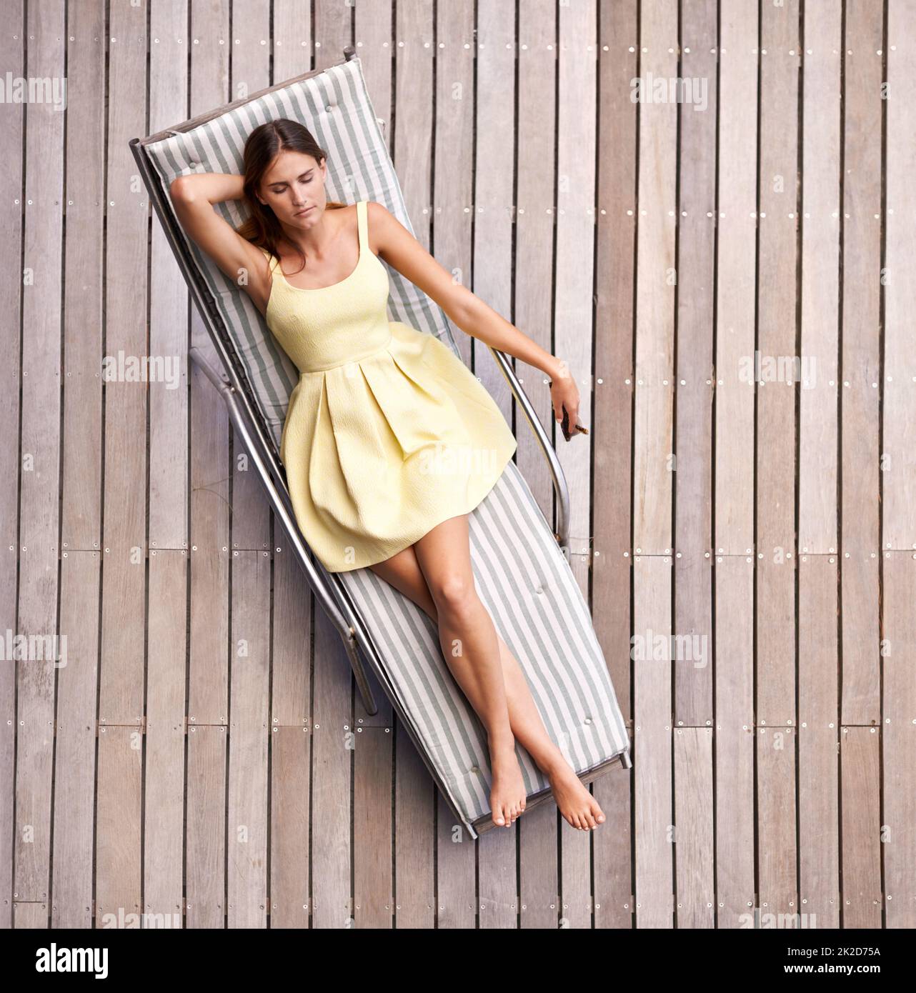 Stilvoll entspannen. Eine junge, wohlhabende Frau, die in einem Sommerkleid auf ihrer Liege liegt. Stockfoto