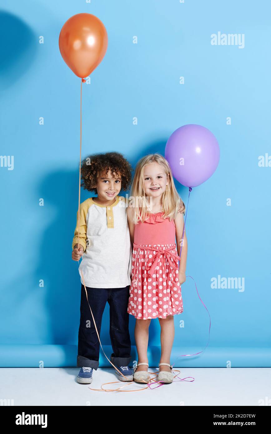 Shes meine Kindheit Schatz. Porträt eines niedlichen kleinen Mädchens und Jungen, der einen Ballon auf einem blauen Hintergrund hält. Stockfoto