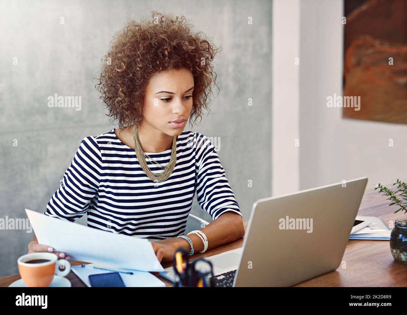 Verwaltung ihrer Papierdokumente und Online-Dokumente. Aufnahme einer jungen Frau, die zu Hause an einem Laptop arbeitet und Papierkram liest. Stockfoto