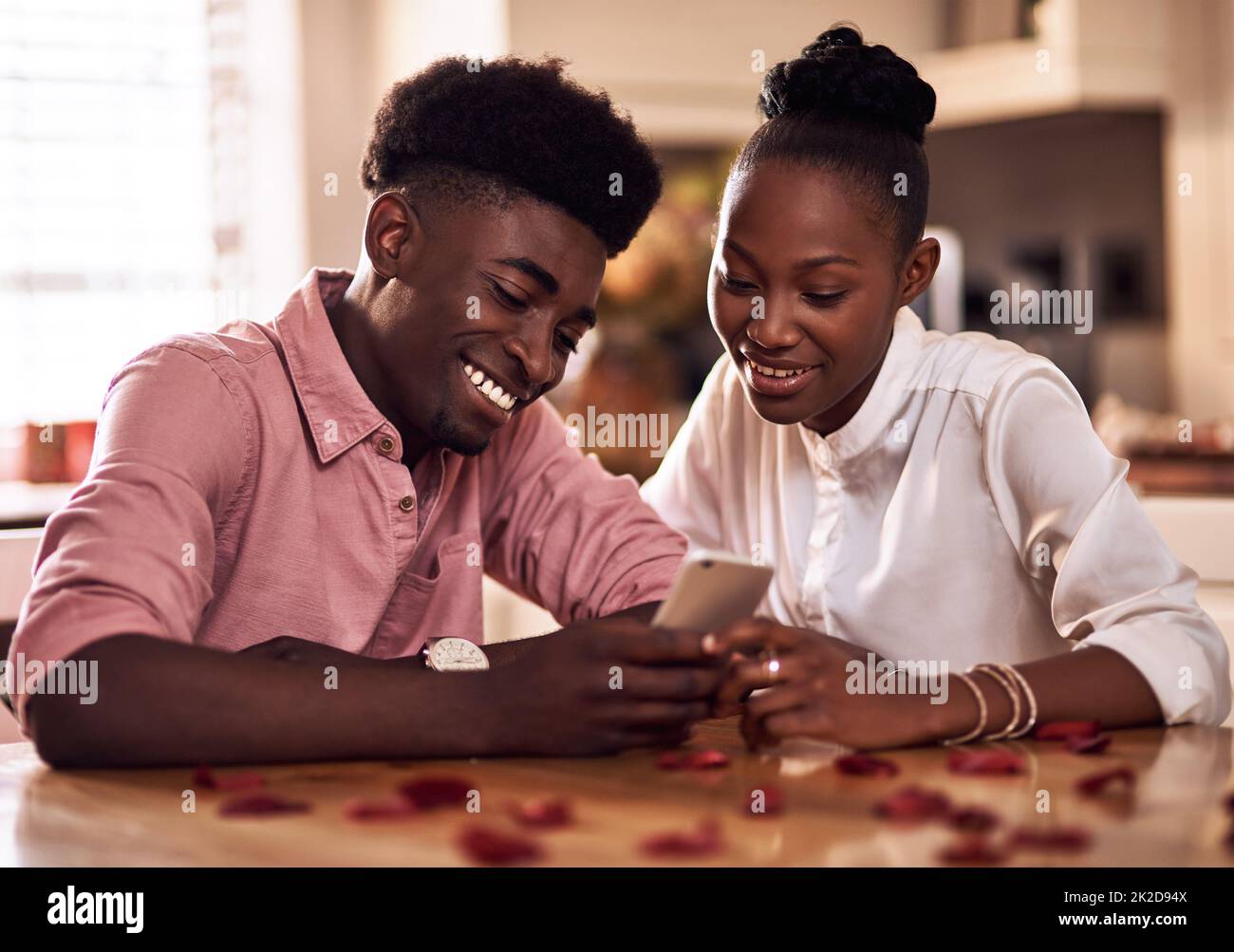Beiträge zum Valentinstag sind bereits im Trend. Eine kurze Aufnahme eines anhänglichen jungen Paares, das ein Smartphone zusammen in seiner Küche zu Hause benutzt. Stockfoto