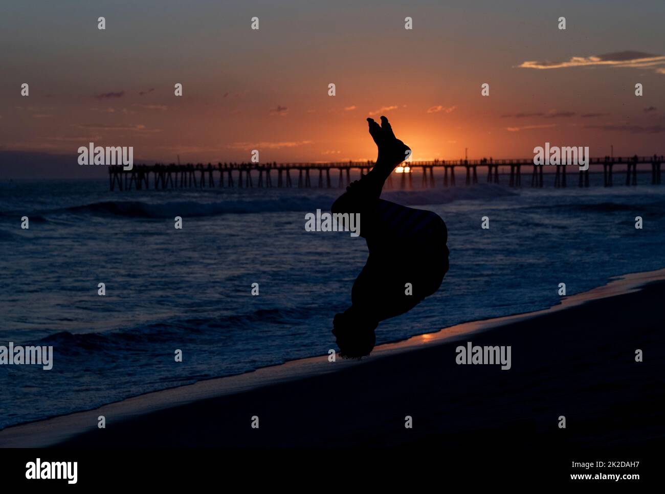 Rückenlehne am Strand bei Sonnenuntergang mit einem Pier im Hintergrund Stockfoto