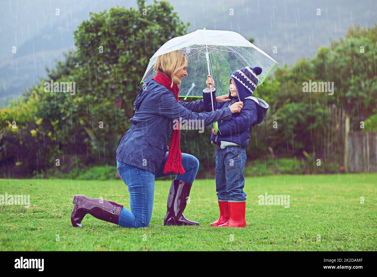 Achten Sie darauf, dass sie verdeckt sind. In voller Länge eine Mutter, die sicherstellt, dass ihr Sohn bedeckt ist, während er draußen im Regen ist. Stockfoto