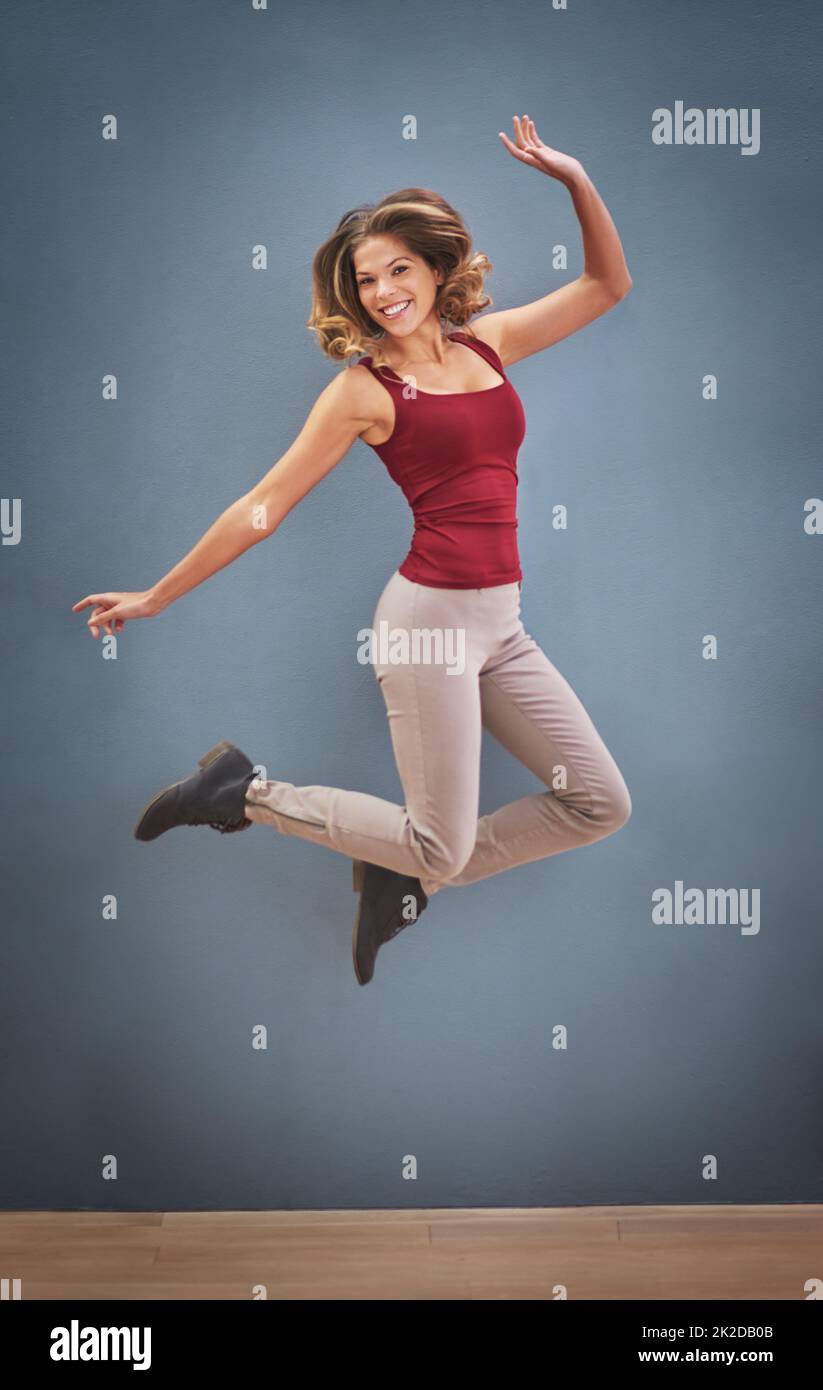 Ohne Fuß und Lust. Aufnahme einer glücklichen jungen Frau, die vor grauem Hintergrund in die Luft springt. Stockfoto