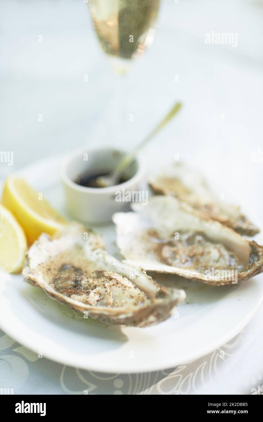 Und zunächst einmal Aufnahme eines Tellers mit Austern, die mit einem Glas Wein auf einem Tisch sitzen. Stockfoto