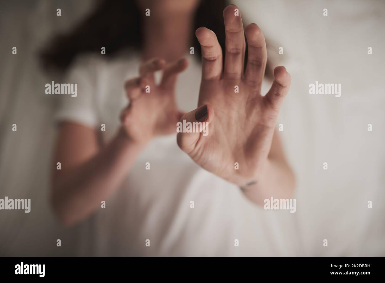 Schadet nicht zuerst. In einem hohen Winkel eine unidentifizierbare junge Frau, die ihre Hände in einer defensiven Geste hochhält, während sie im Bett liegt. Stockfoto