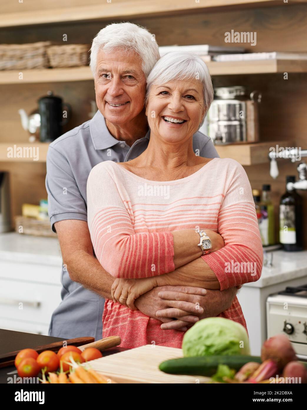 ID tut alles für sie, lernt sogar zu kochen. Aufnahme eines attraktiven Seniorenpaares, das liebevoll in einer Küche posiert. Stockfoto