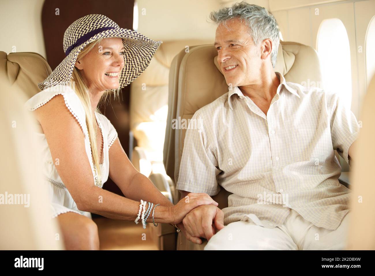 Bereit für einen romantischen Urlaub. Lächelndes Seniorenpaar hält sich die Hände an ein Flugzeug, das nach Übersee fährt. Stockfoto