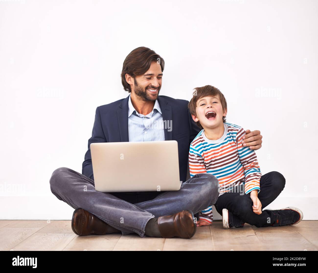 Genießen Sie einige lustige Online-Videos. Ein Vater und ein Sohn sitzen mit einem Laptop auf dem Boden. Stockfoto