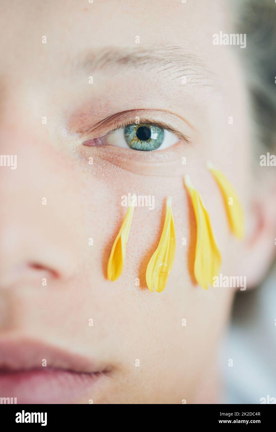 Schönheitsbehandlung. Ausgeschnittene Aufnahme eines jungen mannes mit Blütenblättern unter seinem Auge, während er auf die Kamera schaute. Stockfoto