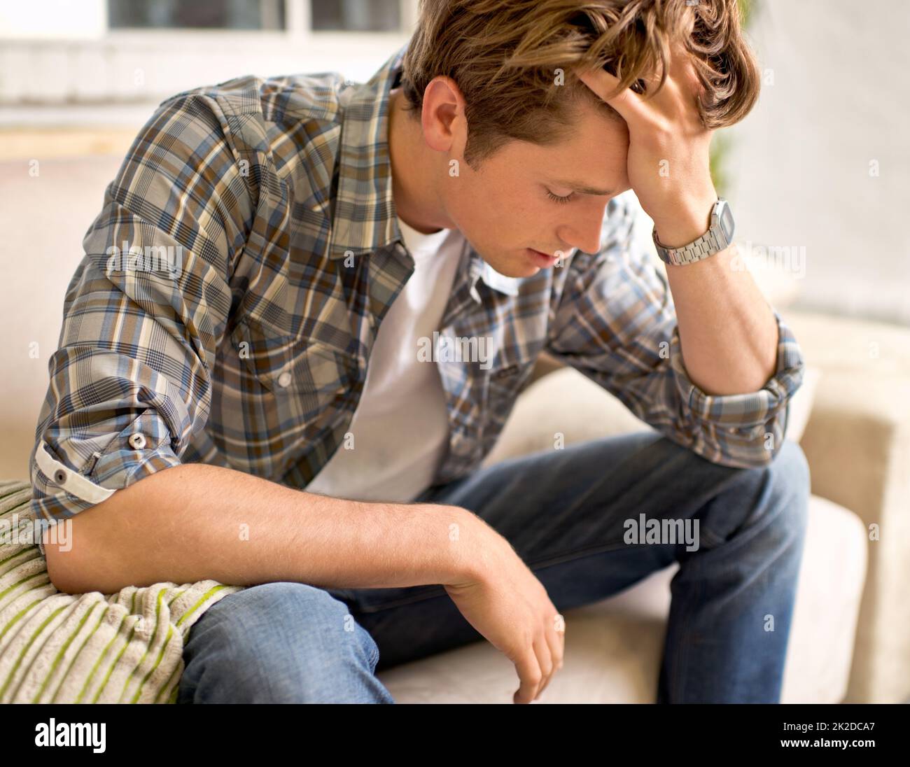 Diese Kopfschmerzen töten mich. Ein junger Mann, der mit der Hand im Haar auf einer Couch sitzt, als ob er Schmerzen hätte. Stockfoto