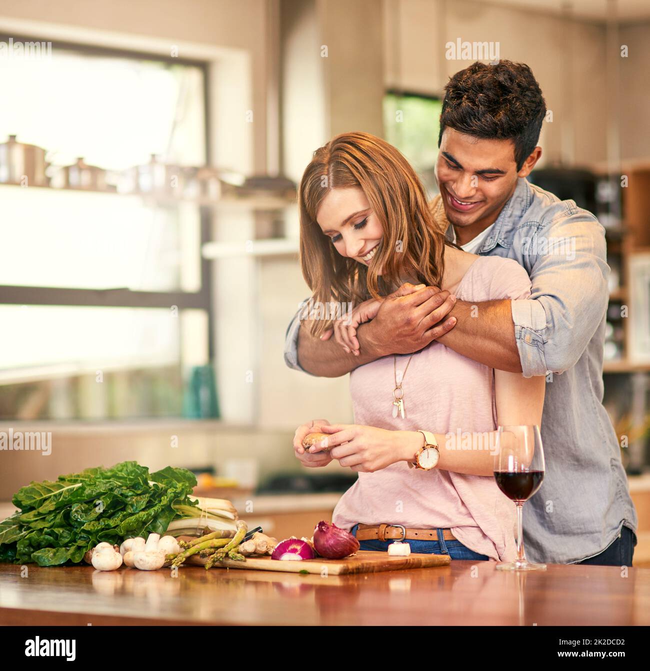 Essen ist Liebe für den Magen. Aufnahme eines jungen Mannes, der seine Frau umarmt, während sie das Abendessen zubereitet. Stockfoto