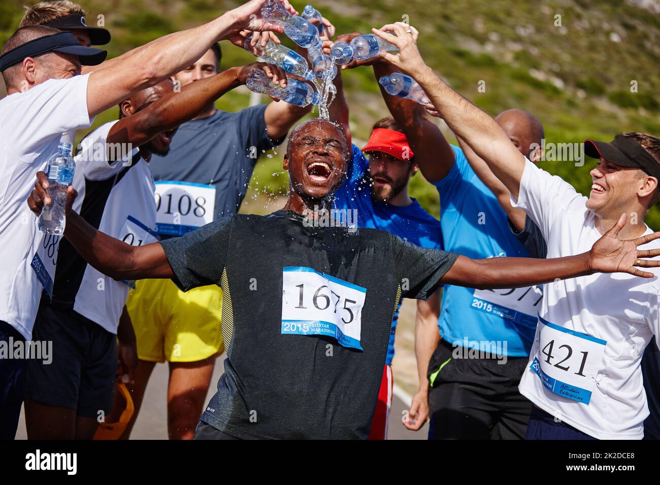 Das war ein unglaubliches Rennen. Aufnahme einer Gruppe junger Männer, die nach einem Marathon Wasser über ihren Freund gießen. Stockfoto