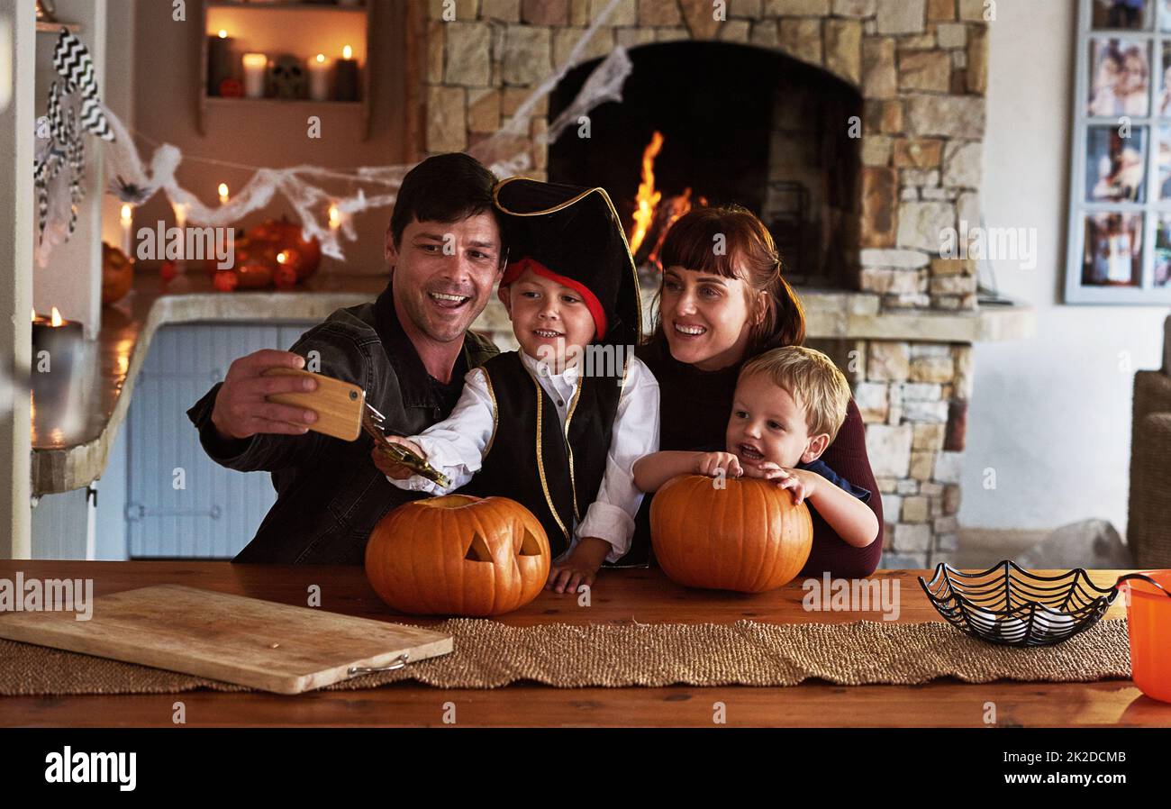 Diese besonderen Momente verdienen es, festgehalten zu werden. Aufnahme einer entzückenden jungen Familie, die zusammen mit einem Handy an halloween zu Hause Selfies macht. Stockfoto