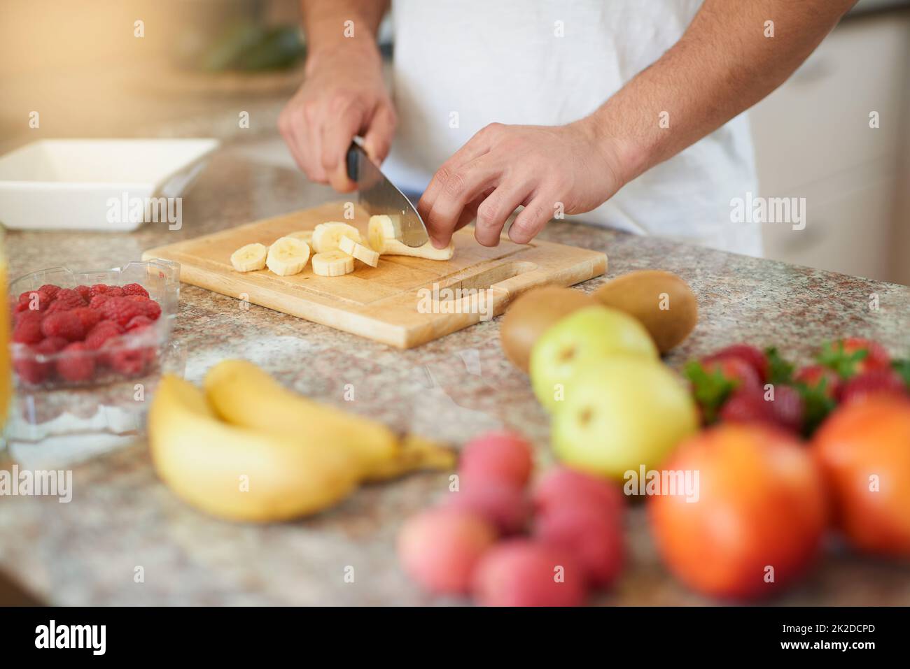 Senden Sie gesunde Gedanken Ihren Weg. Eine kleine Aufnahme eines jungen Mannes, der in seiner Küche einen Obstsalat zubereitet. Stockfoto