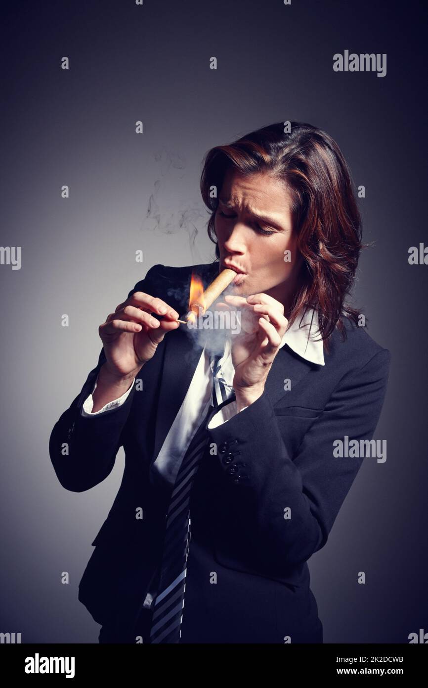 Zeit zum Aufleuchten. Eine Geschäftsfrau in Anzug und Krawatte, während sie eine Zigarre anzünden. Stockfoto