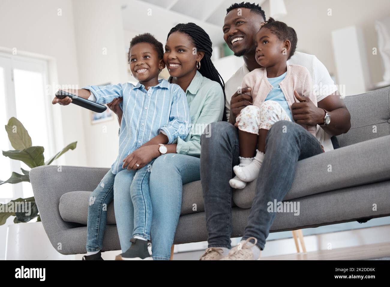 Was ist im Fernsehen zu sehen? Low-Angle-Aufnahme einer liebevollen jungen vierköpfigen Familie, die zu Hause im Wohnzimmer Fernsehen schaut. Stockfoto