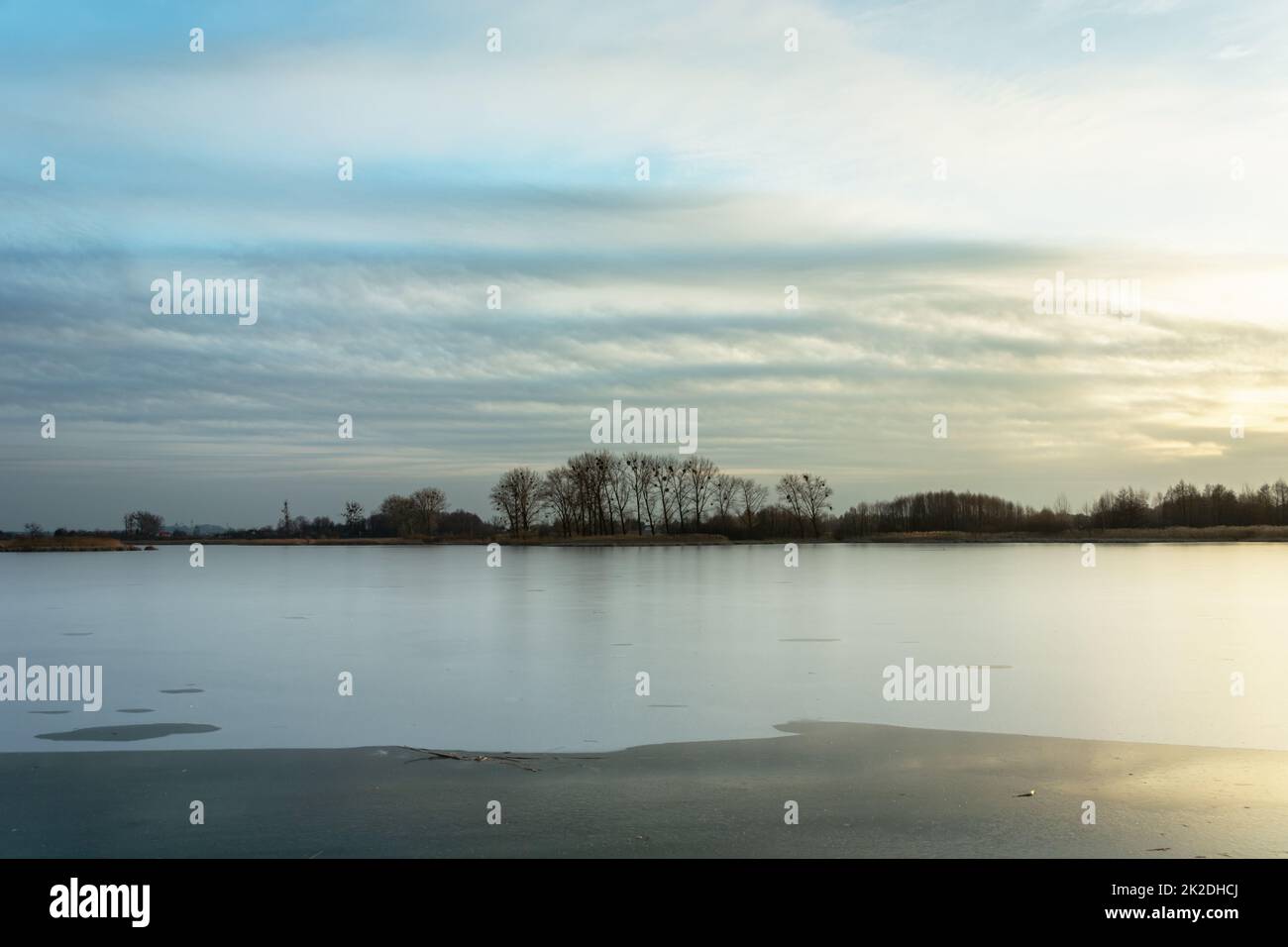 Gefrorener See, Bäume am Ufer und Wolken Stockfoto