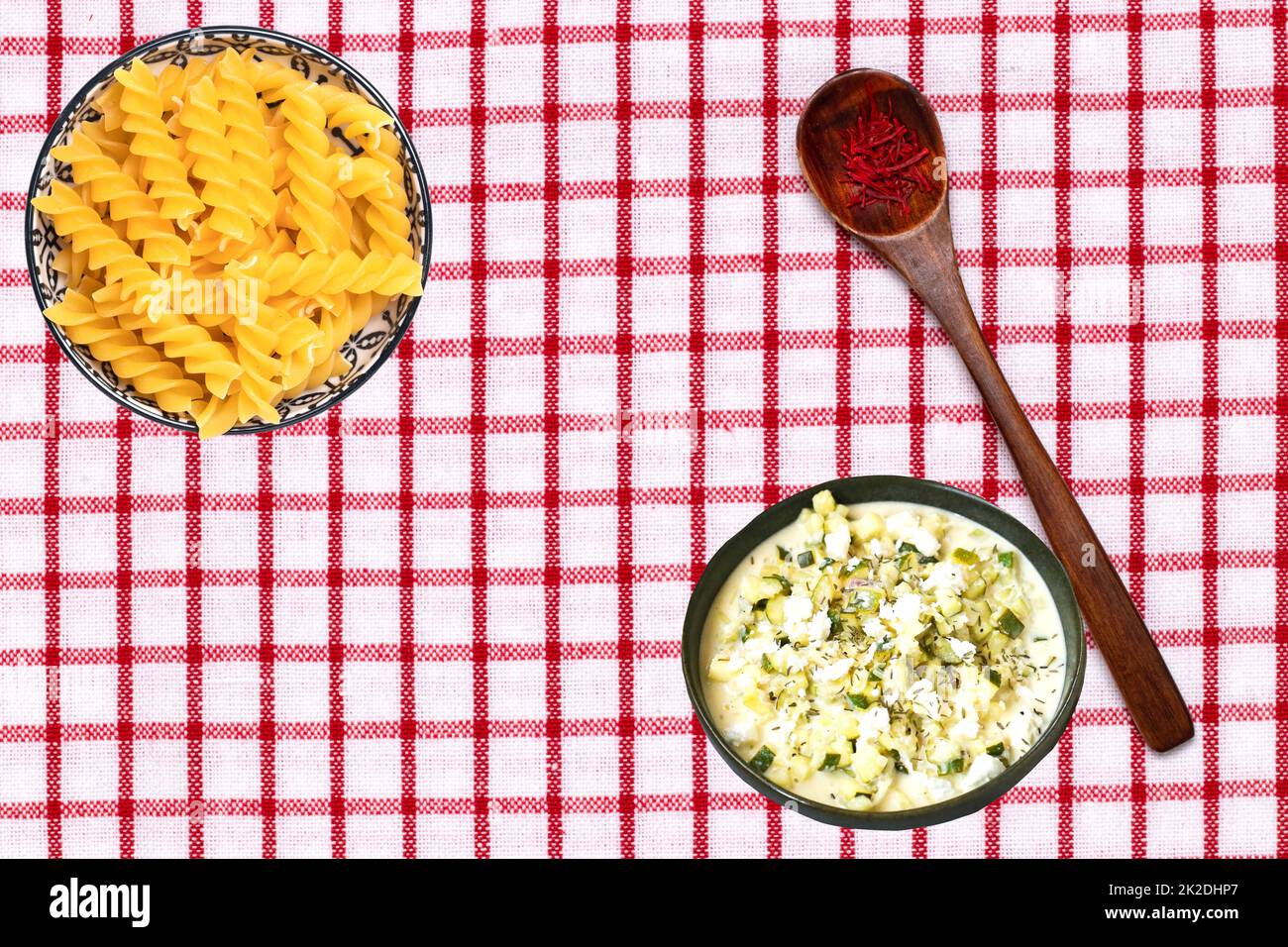 Gemüsesaatgut. Zwei Schüsseln mit Nudeln und griechischer Suppe und ein Löffel mit safran Gewürzfäden auf einer Tischdecke. Gesunde Ernährung. Draufsicht mit Platz. Stockfoto