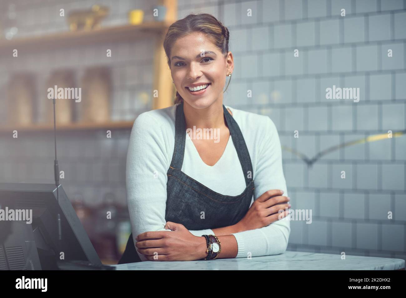 Was kann ich für Euch bekommen? Porträt einer jungen Frau, die hinter der Theke ihres Ladens arbeitet. Stockfoto