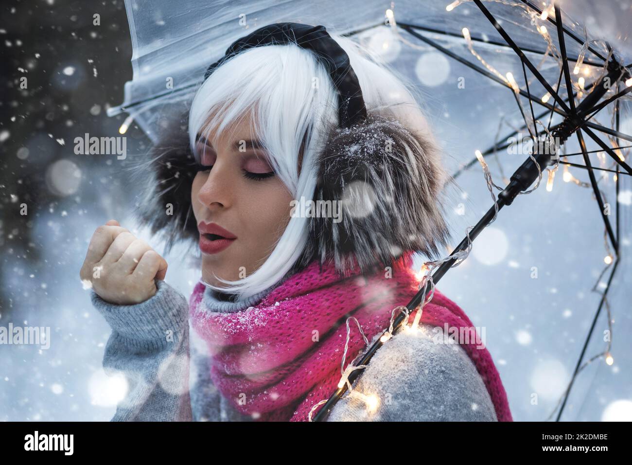 Junge Frau, die am verschneiten Wintertag unter einem transparenten Regenschirm läuft Stockfoto