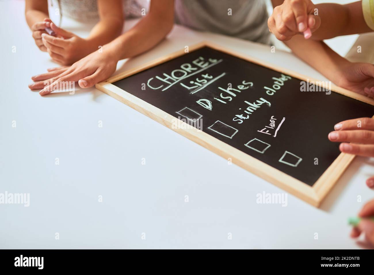 Auflisten ihrer Aufgaben. Nahaufnahme von Kindern, die zu Hause eine Liste der Aufgaben auf einer Tafel schreiben. Stockfoto