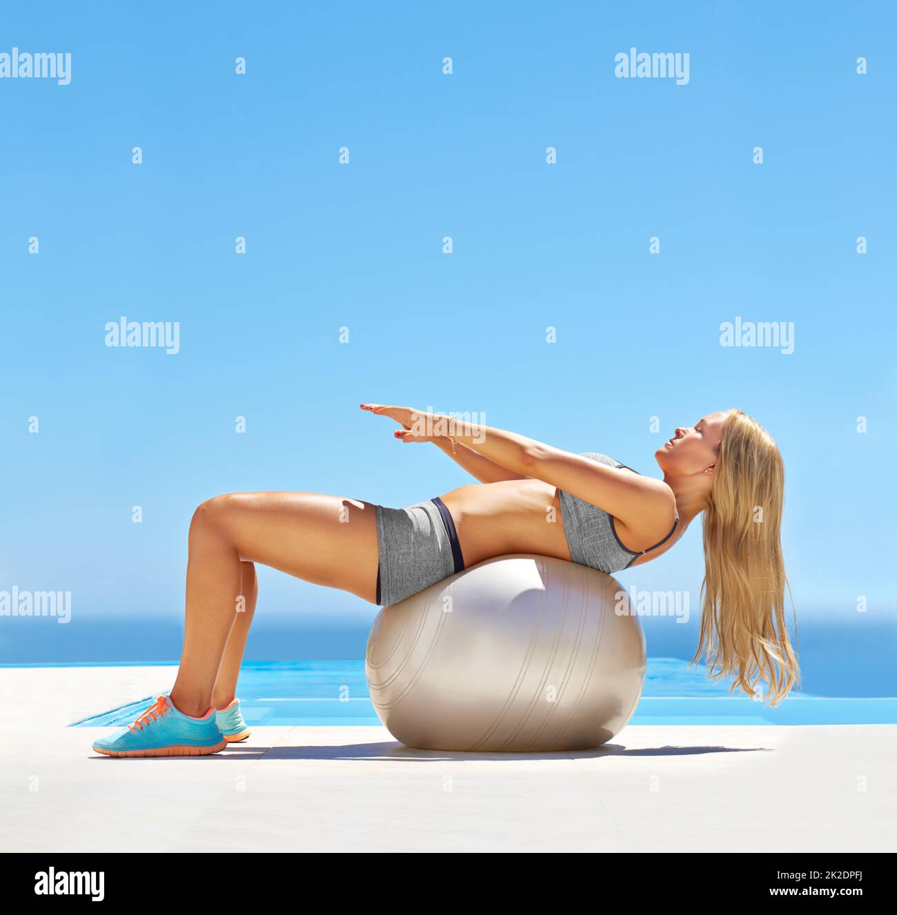 Straffen Sie den Bauch. Aufnahme einer attraktiven jungen Frau, die mit einem Gymnastikball am Pool trainiert. Stockfoto