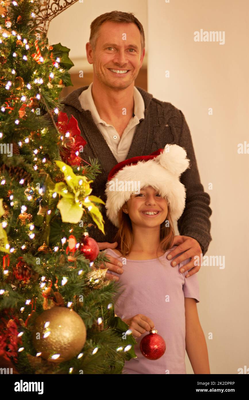 Das perfekte Finish.... Ein Vater und seine junge Tochter schmücken den weihnachtsbaum zu Hause. Stockfoto