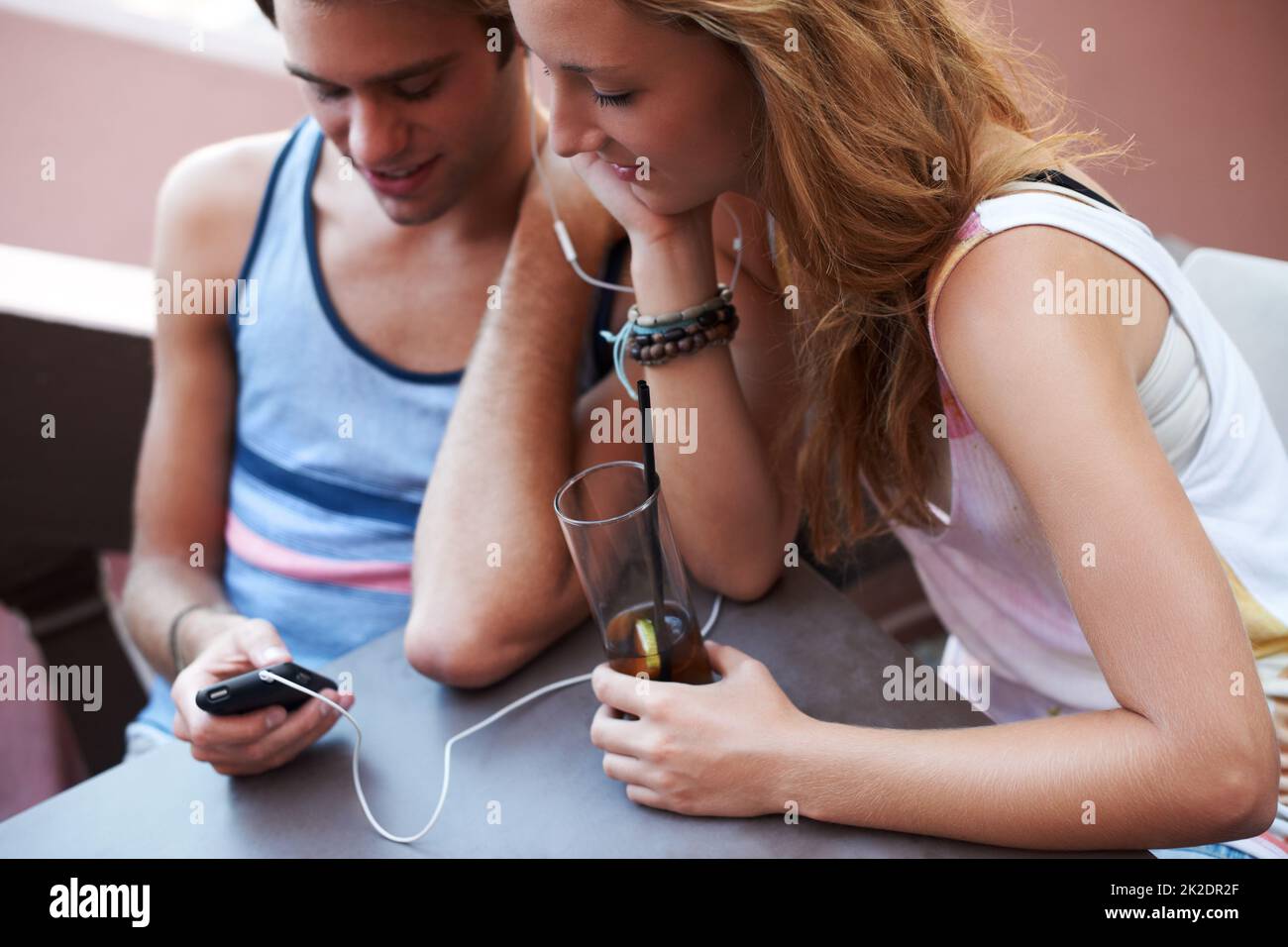 Kommen Sie Ihrem Schwarm näher durch die Wunder der Technologie. Glückliches Teenager-Paar, das sich einen MP3-Player teilt und Musik hört, während es seine Getränke genießt. Stockfoto