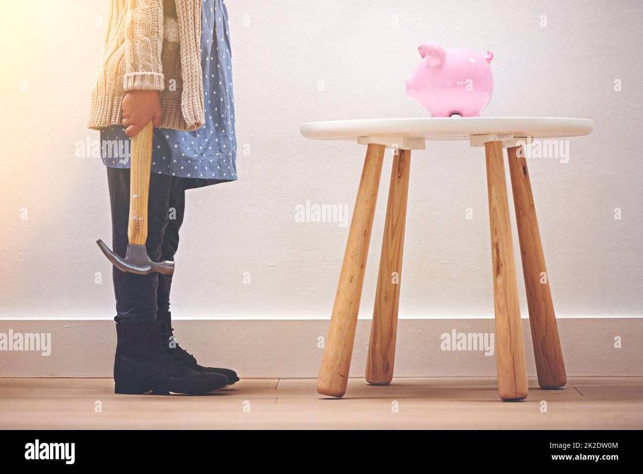 Einen frühen Start in ihre Ersparnisse zu bekommen. Ein kleines Mädchen, das mit einem Hammer neben ihrem Sparschwein steht. Stockfoto
