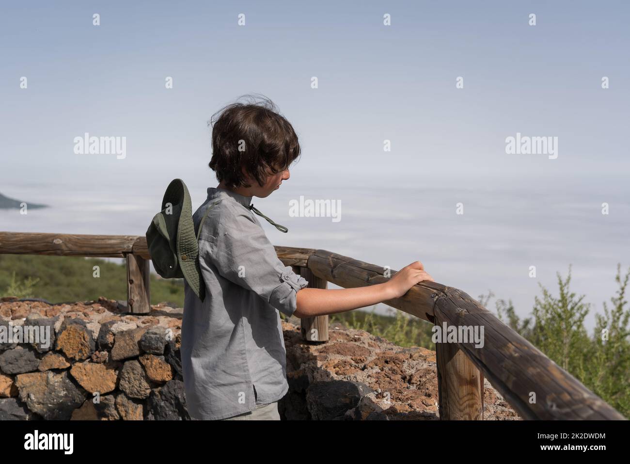 Ein Teenager steht auf einer Aussichtsplattform hoch in den Bergen und blickt in die Ferne. Stockfoto