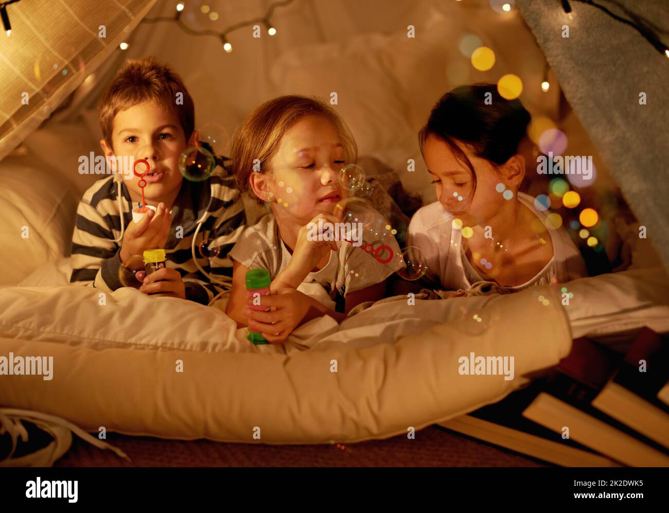 Camping im Schlafzimmer. Aufnahme von drei kleinen Kindern in einer Decke Fort Blasen blasen. Stockfoto