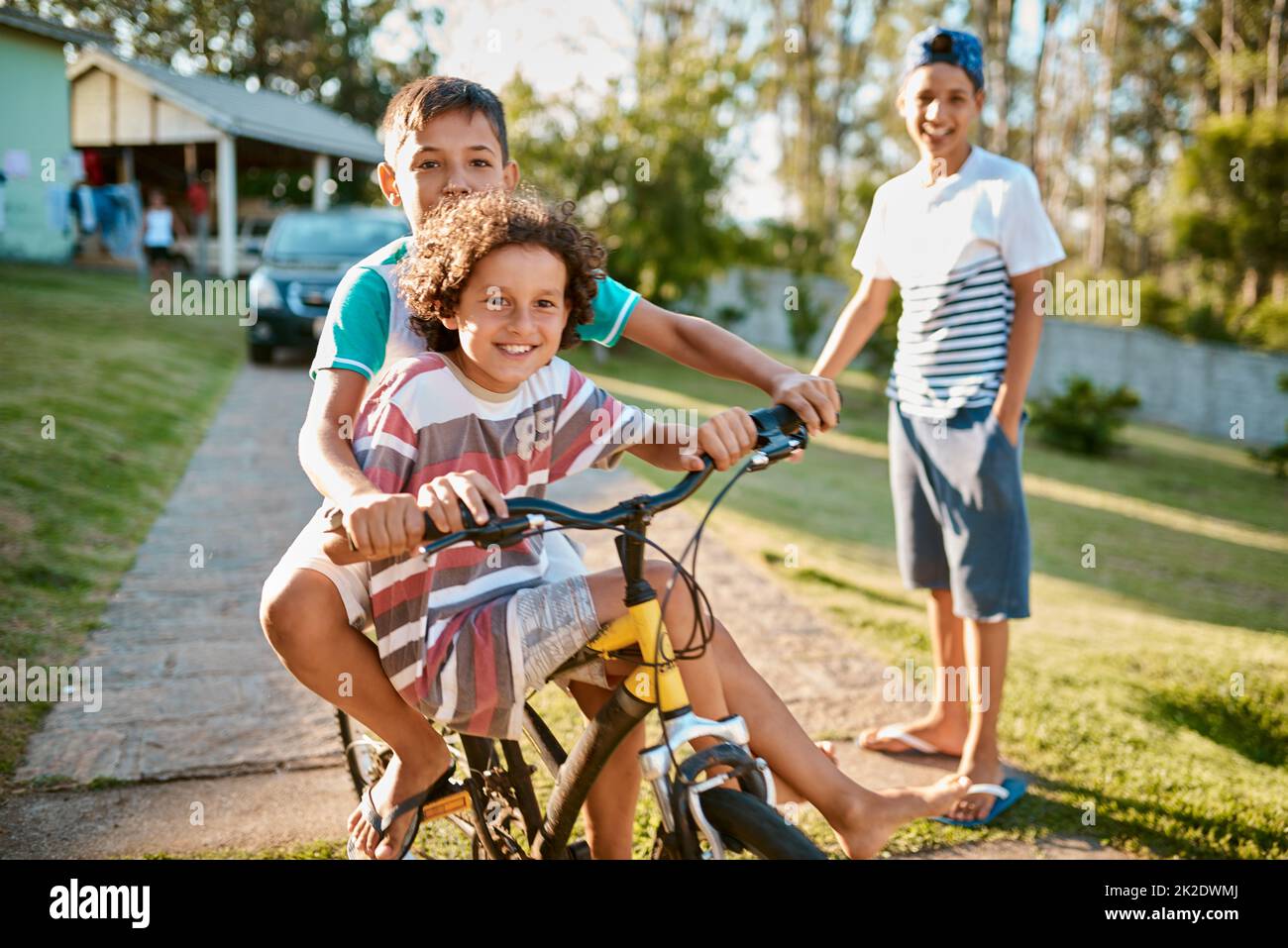 Erste Regel der Brüderlichkeit Fahren Sie gemeinsam mit dem Fahrrad. Aufnahme von glücklichen jungen Brüdern, die gemeinsam in ihrem Hinterhof ein Fahrrad fahren. Stockfoto