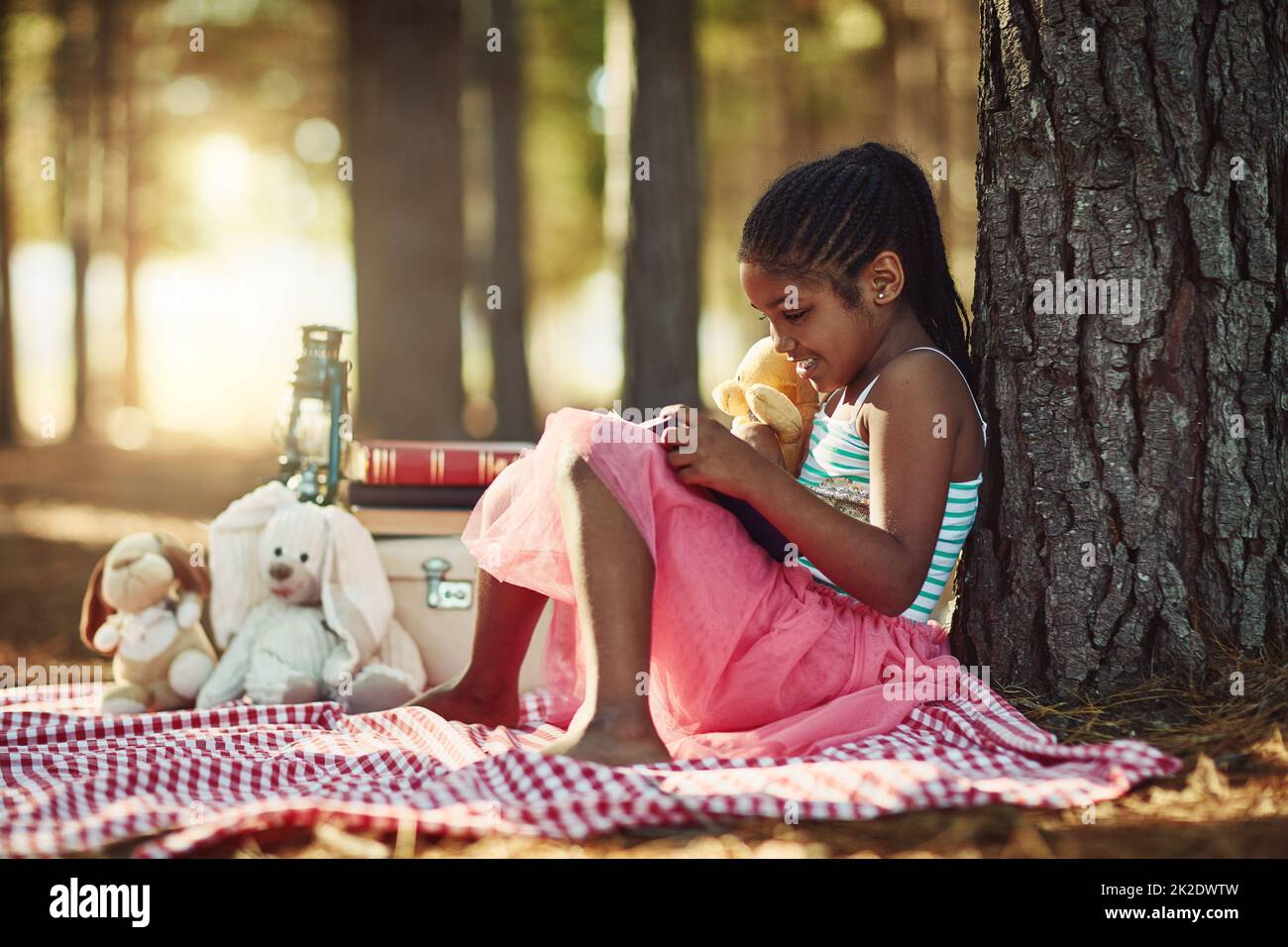 Story Time mit ihrem Lieblings-Teddy. Aufnahme eines kleinen Mädchens, das mit ihren Spielsachen im Wald ein Buch liest. Stockfoto