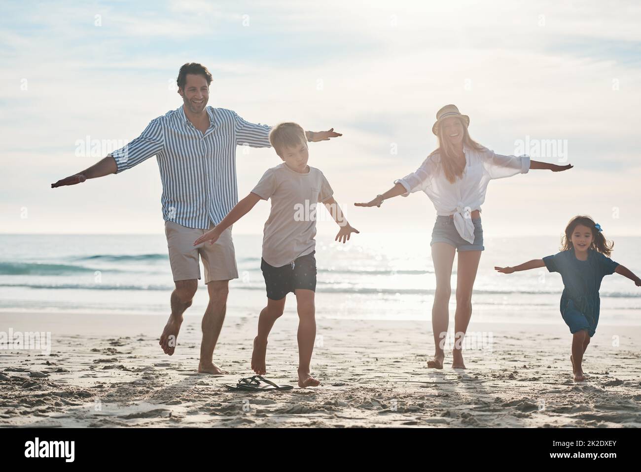 Es ist ein Rennen. Die ganze Aufnahme eines glücklichen jungen Paares, das mit seinen beiden Kindern einen verspielten Tag am Strand genießt. Stockfoto
