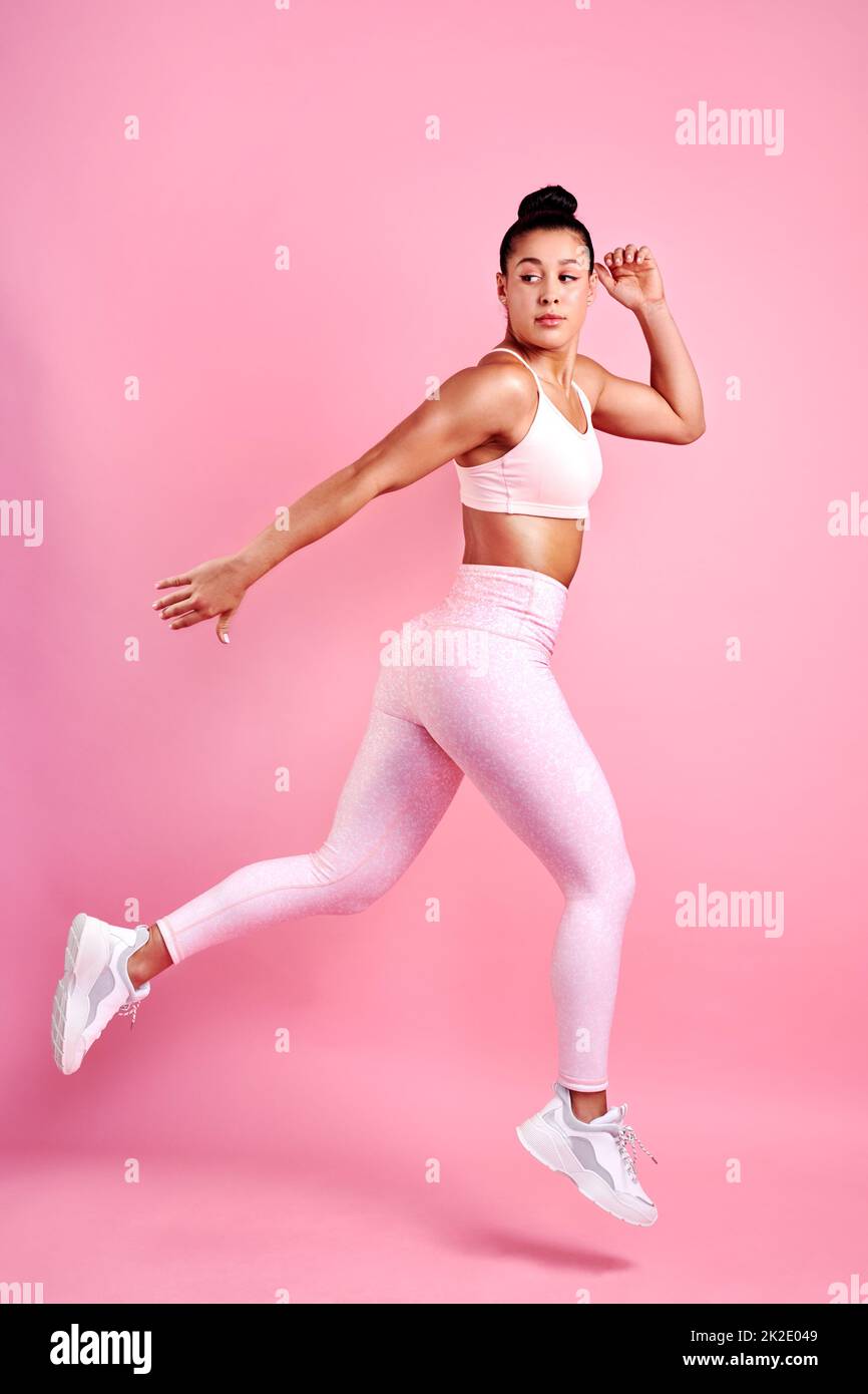 Ich werde mich weiterhin einschalten. Studioaufnahme einer sportlichen jungen Frau, die vor einem rosa Hintergrund springt. Stockfoto