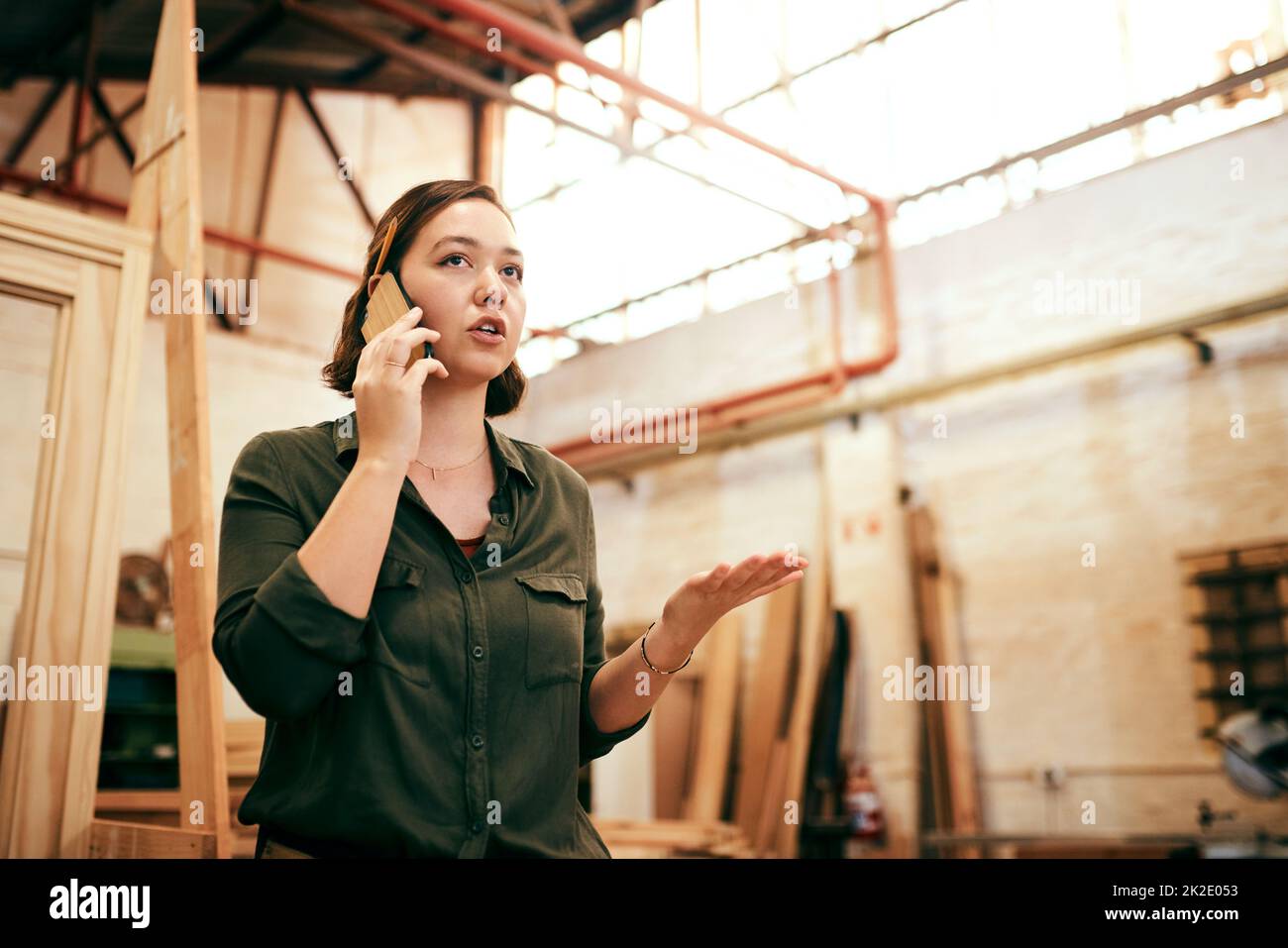 Ich habe immer neue Bestellungen. Aufnahme einer Tischlerin, die auf ihrem Handy sprach, während sie in ihrer Werkstatt stand. Stockfoto