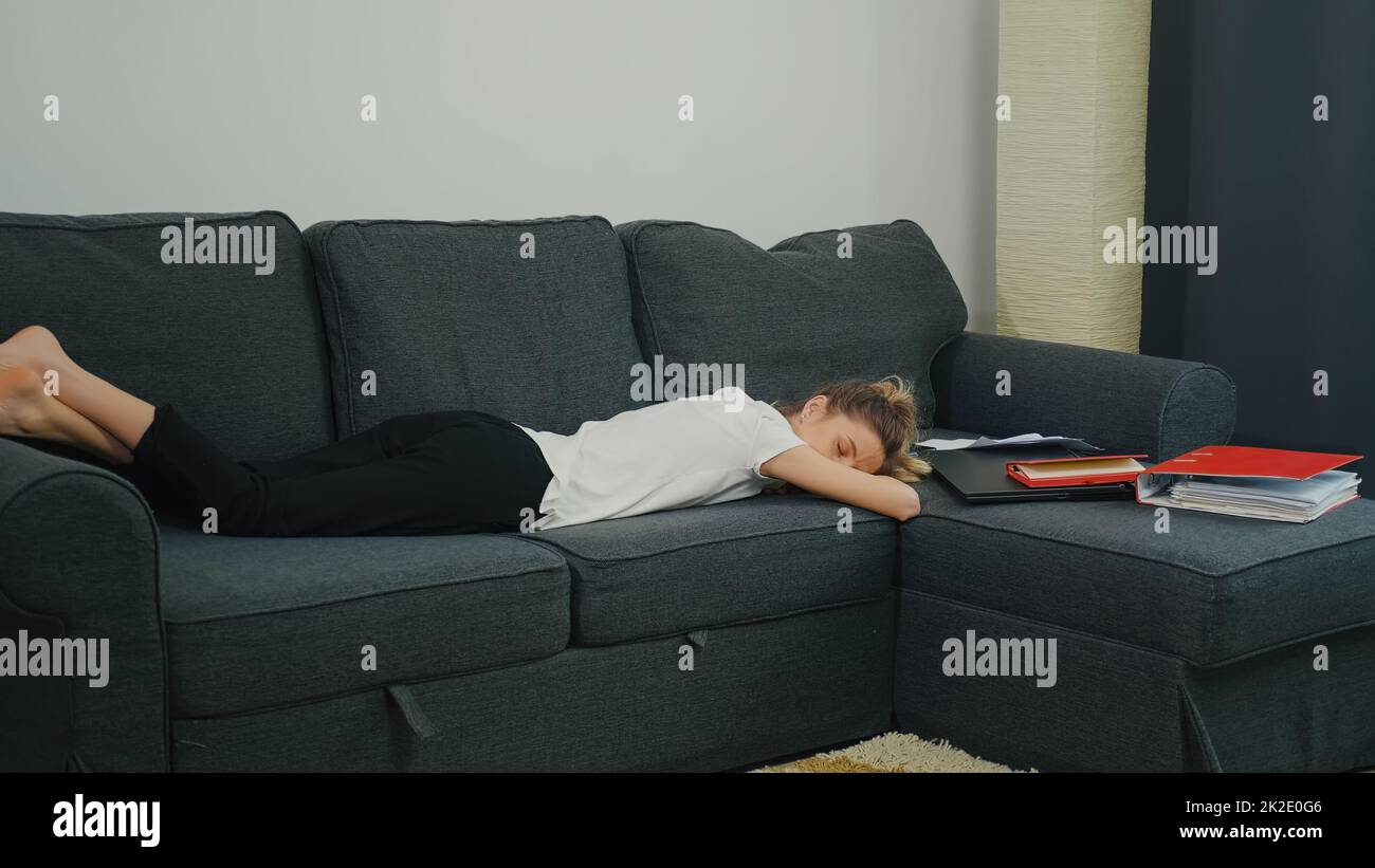 Erste Berufserfahrung. Die junge Frau schlief nach einem harten Arbeitstag auf der Couch neben Laptop und Büropapieren. Stockfoto