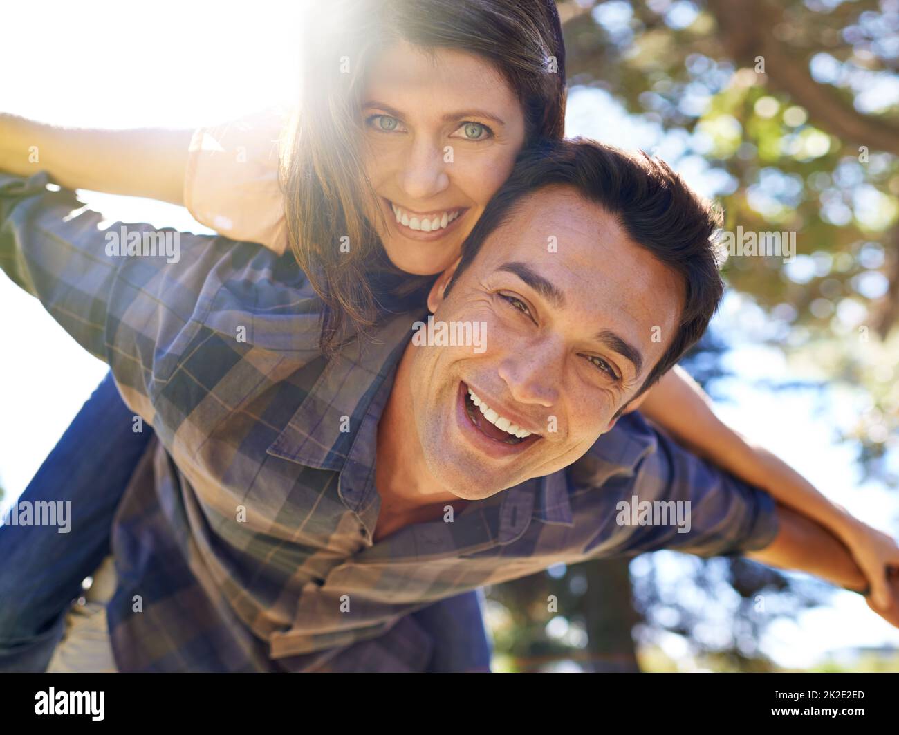 Verspielt und verliebt. Aufnahme eines Mannes, der seinen Partner auf dem Rücken im Park trägt. Stockfoto