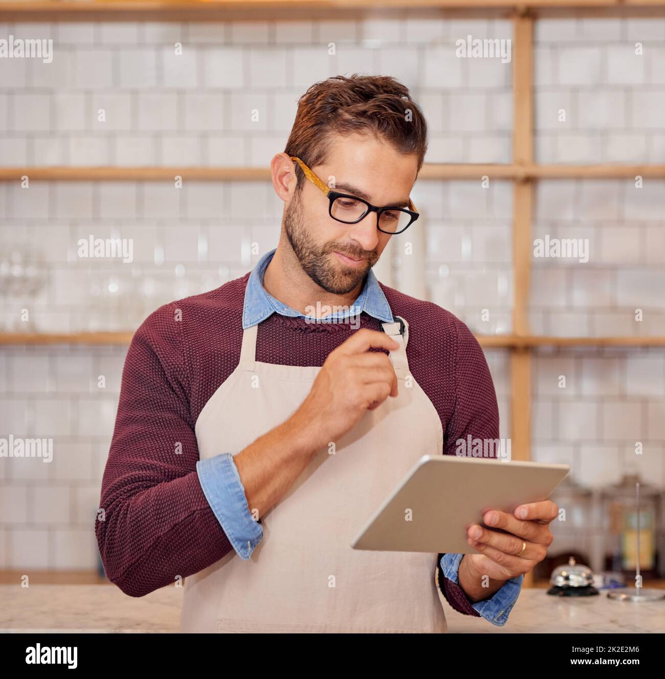 Einige Änderungen am Online-Menü vornehmen. Aufnahme eines glücklichen jungen Geschäftsbesitzers, der ein Tablet benutzte, während er in seinem Café stand. Stockfoto