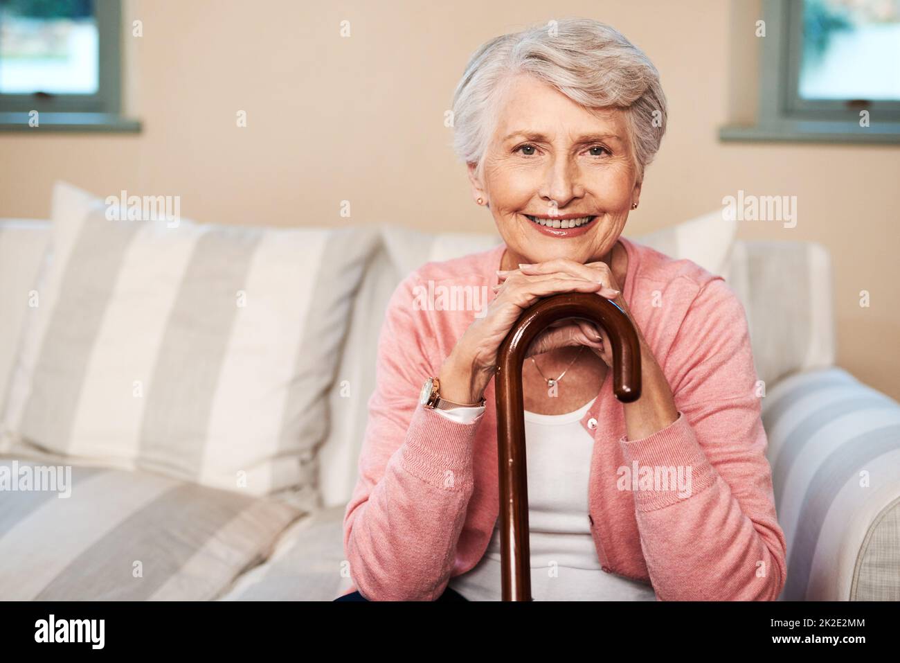 Das Leben ist so schön, wie du es machst. Porträt einer älteren Frau, die mit einem Spazierstock zu Hause sitzt. Stockfoto