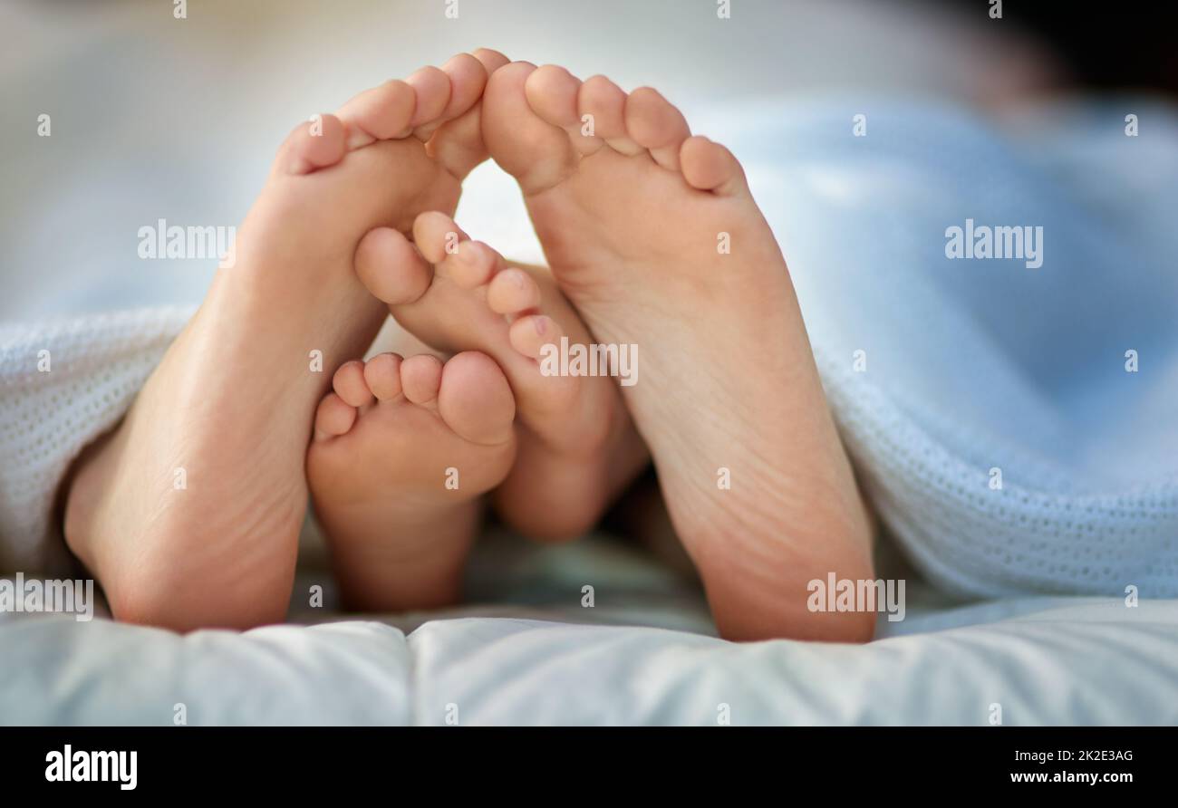 Deine winzigen Zehen und meine. Zugeschnittenes Bild von den Füßen eines Elternteils und eines Kindes, die unter den Abdeckungen herausragen. Stockfoto