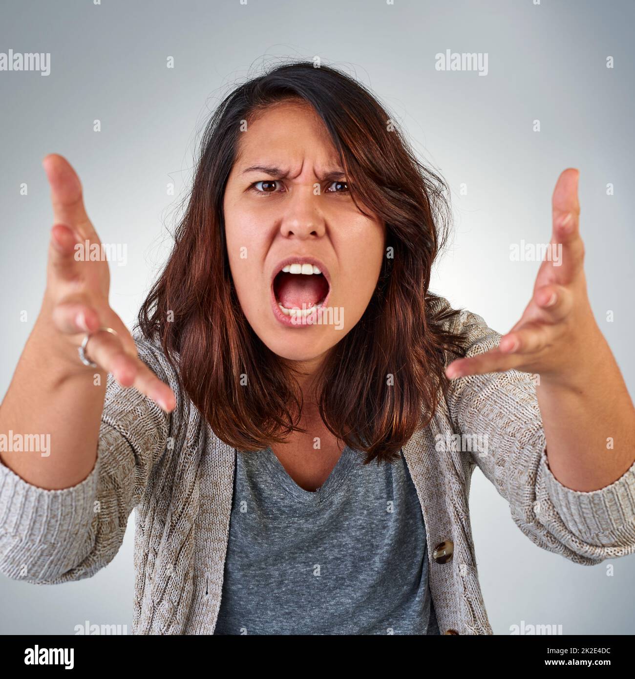 Wie könnten Sie das tun? Porträt einer wütenden jungen Frau, die vor grauem Hintergrund schreit. Stockfoto