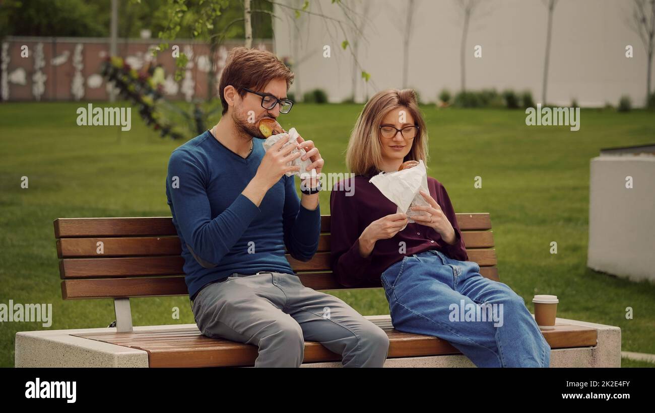 Junge Geschäftsleute, die in einem Park einen Snack mit Essen zum Mitnehmen genießen. Essen im Freien. Essen genießen. Riecht nach guten Snacks. Stockfoto