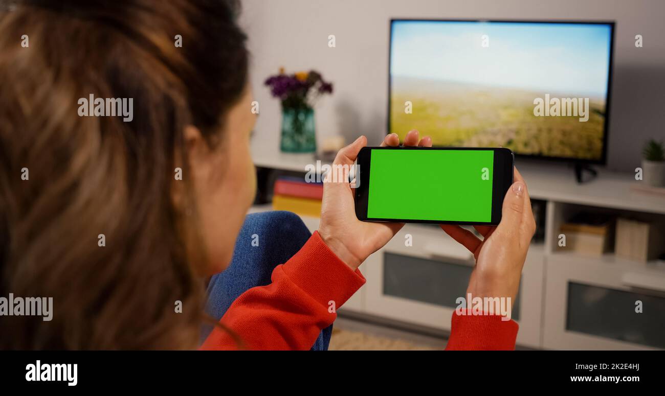 Horizontaler grüner Bildschirm für Copy Space Close Up Chroma Key Mockup. Zurück über die Schulter View Girl sieht sich einen Film auf Couch Home an. Benutzer von Handyhaltetechnologie. Stockfoto