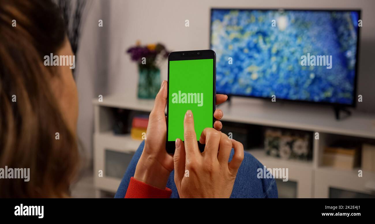 Frau, die ein Smartphone mit grünem Bildschirm für Copy Space Chroma Key Mock Up mit Trackingmarkierungen und Alpha Matte verwendet. Berühren Sie Geste. Gadget ansehen und Make Touch auf dem Bildschirm. Ansicht über der Schulter. Stockfoto