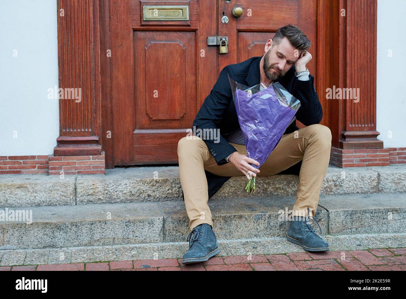 Angesichts der kalten Schulter. Aufnahme eines hübschen jungen Mannes, der deprimiert aussieht, während er mit einem Blumenstrauß auf einer Stufe wartet. Stockfoto