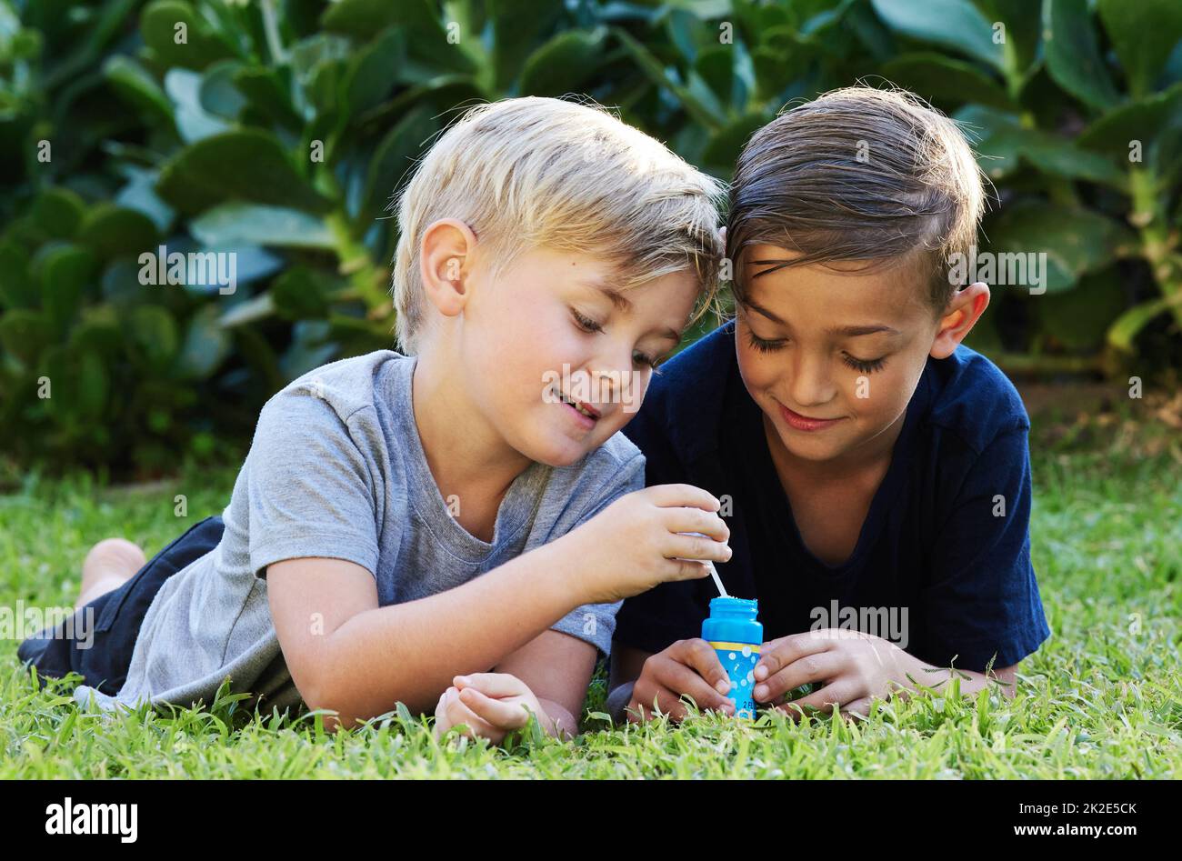 Bleiben Sie wild, Sie werden älter, bitte nicht erwachsen. Aufnahme von zwei entzückenden Jungen, die mit Blasen auf dem Gras im Hinterhof spielen. Stockfoto